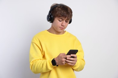 Photo of Cute teenage boy in headphones with smartphone on light grey background