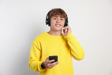 Photo of Portrait of smiling teenage boy in headphones with smartphone on light grey background