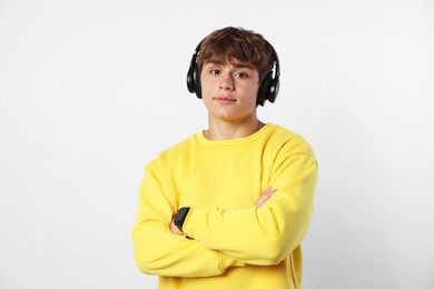 Photo of Portrait of cute teenage boy in headphones with crossed arms on light grey background