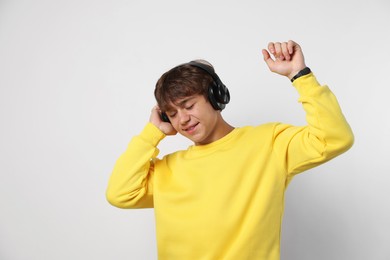 Photo of Smiling teenage boy in headphones enjoying music on light grey background