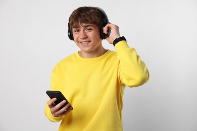 Photo of Portrait of smiling teenage boy in headphones with smartphone on light grey background