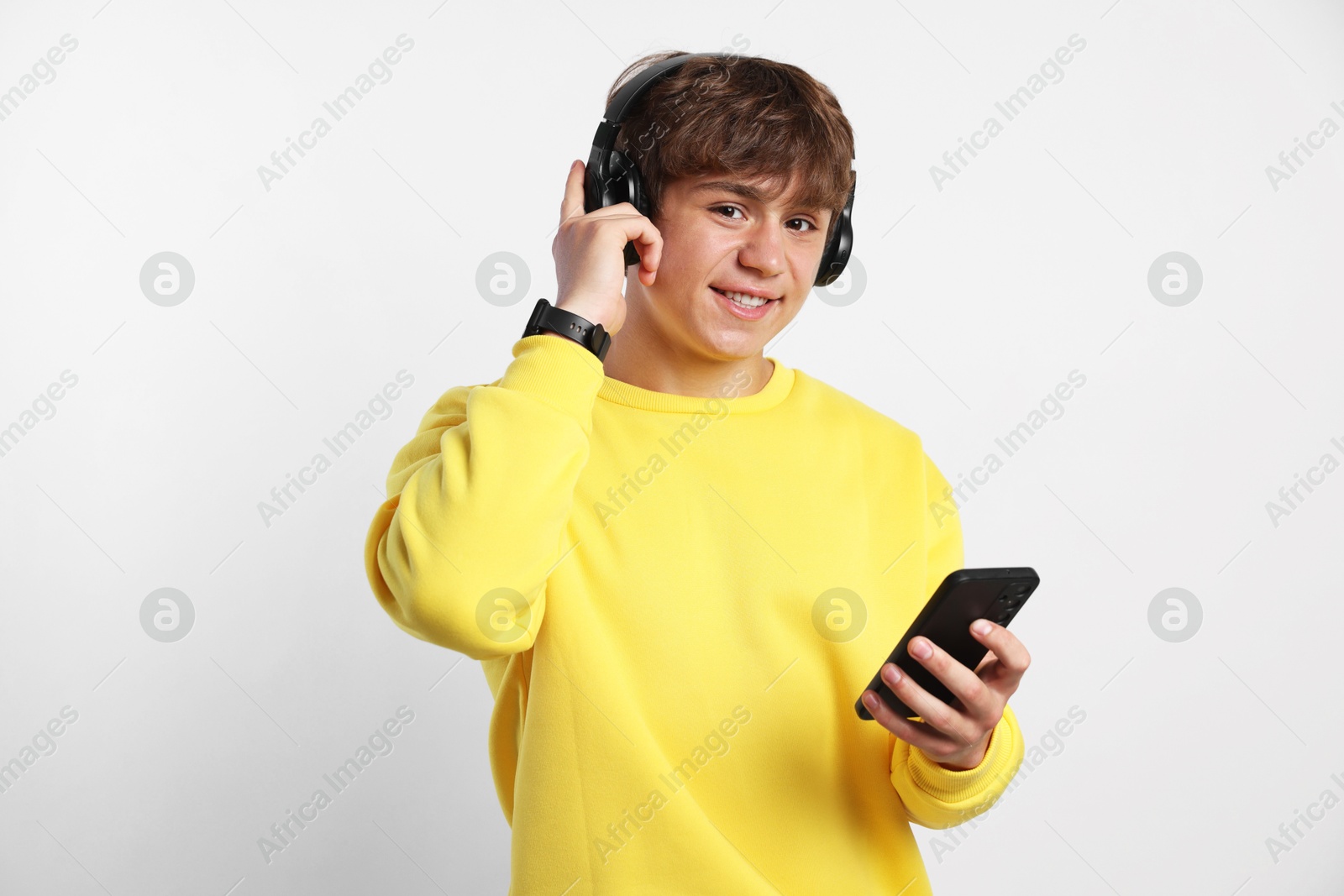 Photo of Portrait of smiling teenage boy in headphones with smartphone on light grey background