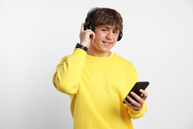 Photo of Portrait of smiling teenage boy in headphones with smartphone on light grey background