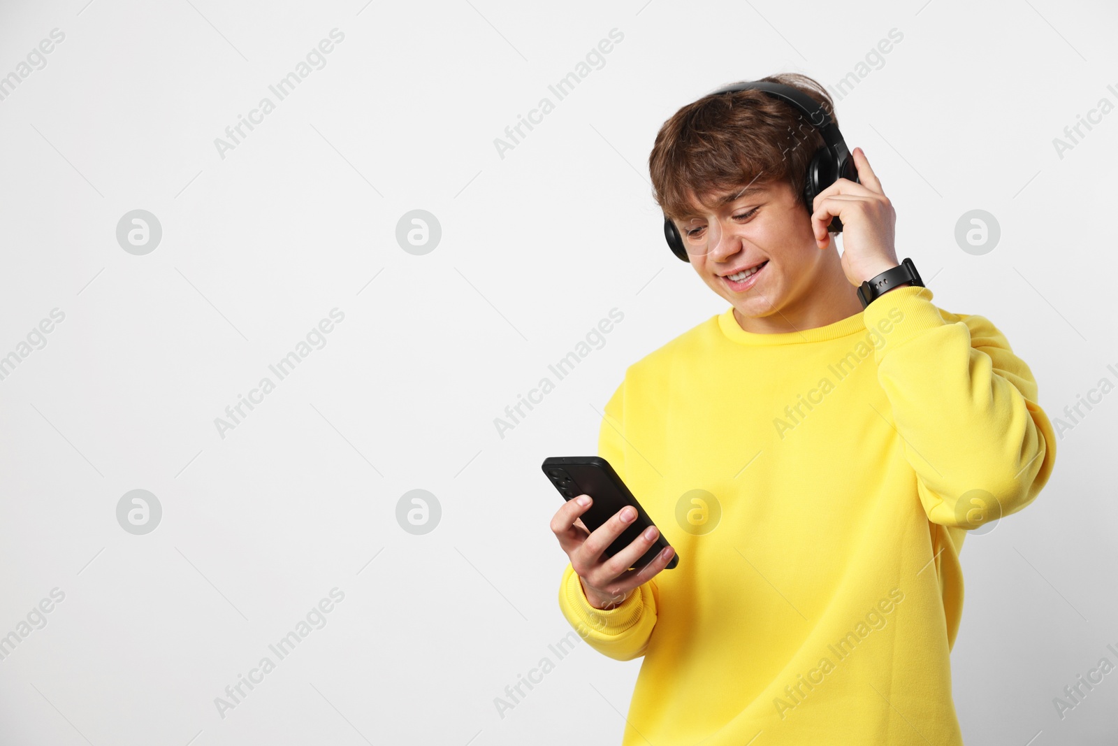 Photo of Smiling teenage boy in headphones with smartphone on light grey background. Space for text
