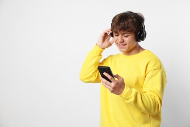 Photo of Smiling teenage boy in headphones with smartphone on light grey background. Space for text