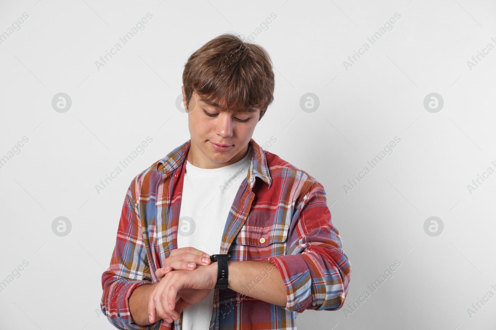 Photo of Cute teenage boy looking at wristwatch on light grey background