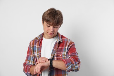 Photo of Cute teenage boy looking at wristwatch on light grey background