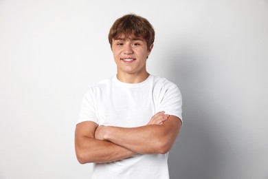 Photo of Portrait of smiling teenage boy with crossed arms on light grey background