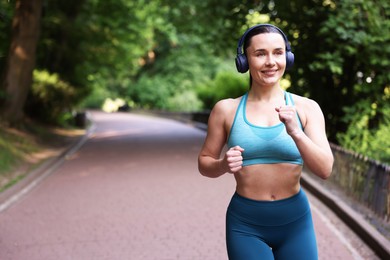 Photo of Sporty woman with headphones running in park, space for text