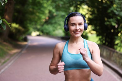 Photo of Sporty woman with headphones running in park, space for text
