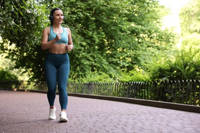 Photo of Sporty woman with headphones running in park, space for text