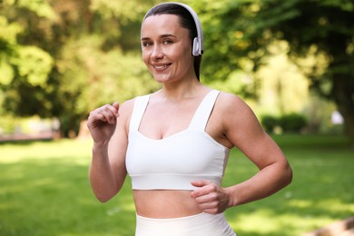 Photo of Sporty woman with headphones running in park