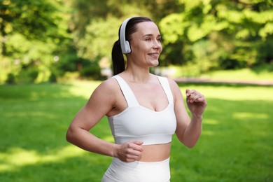 Photo of Sporty woman with headphones running in park