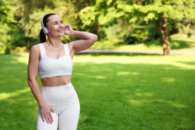 Photo of Woman in sportswear and headphones in park, space for text