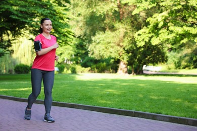 Photo of Sporty woman with armband running in park, space for text