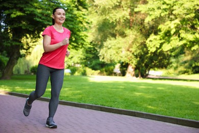 Photo of Sporty woman with armband running in park, space for text