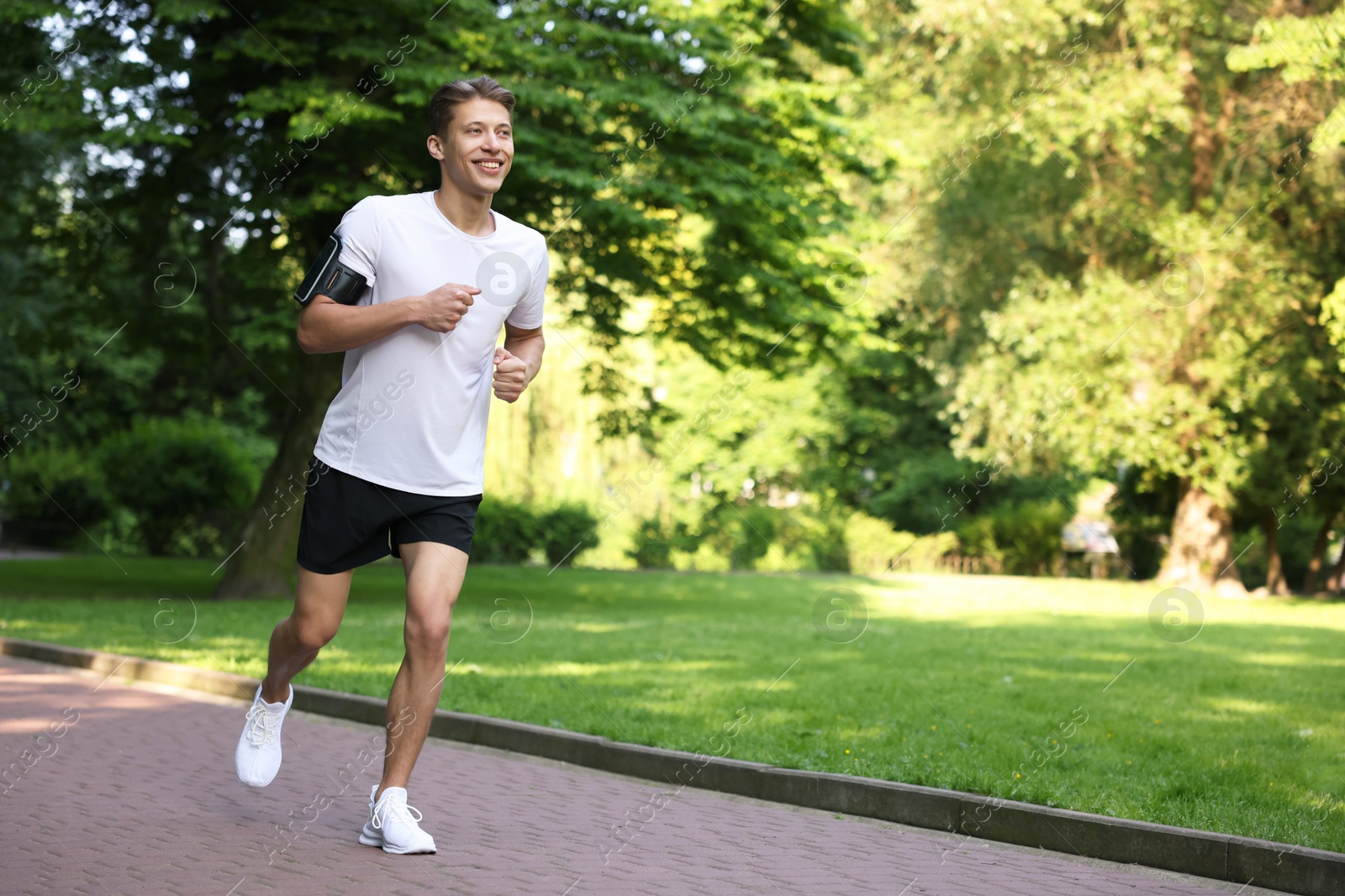 Sporty man with armband running in park, space for text Photo of Sporty man with armband running in park, space for text