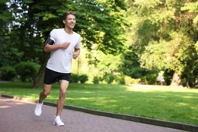 Photo of Sporty man with armband running in park, space for text