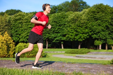 Photo of Sporty man with headphones running in park, space for text