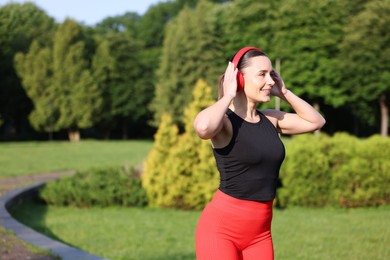 Photo of Sporty woman with headphones running in park, space for text