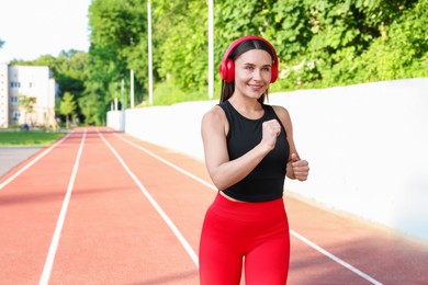 Photo of Sporty woman with headphones running at stadium, space for text