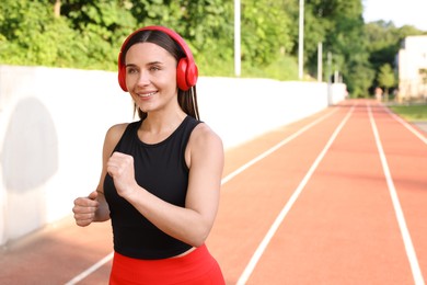 Photo of Sporty woman with headphones running at stadium, space for text