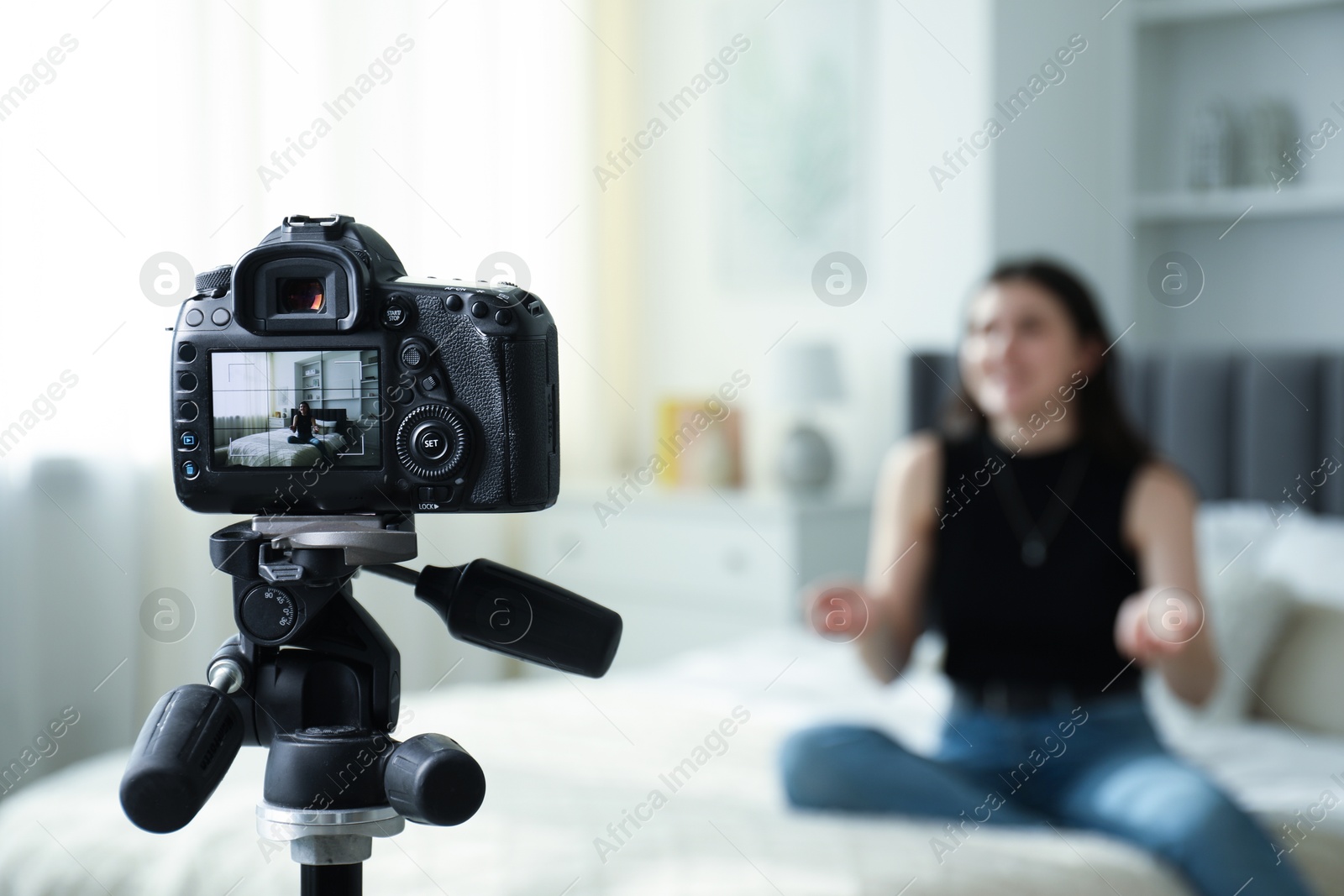 Photo of Woman sitting on bed in studio, focus on video camera recording her