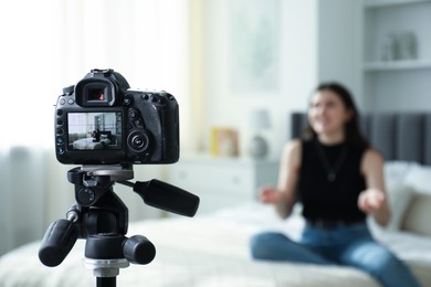 Photo of Woman sitting on bed in studio, focus on video camera recording her