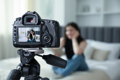 Photo of Woman reading book on bed in studio, focus on video camera recording her