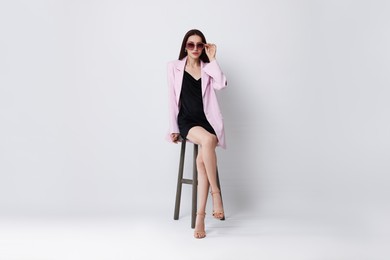 Photo of Beautiful woman in stylish outfit sitting on chair against white background