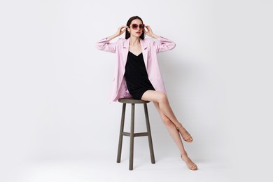 Photo of Beautiful woman in stylish outfit sitting on chair against white background