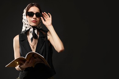 Photo of Beautiful woman in stylish outfit with fashion magazine on black background, space for text