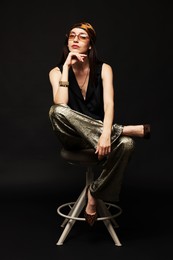 Photo of Beautiful woman in stylish outfit sitting on chair against black background