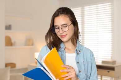 Photo of Beautiful teenage girl with notepads at home