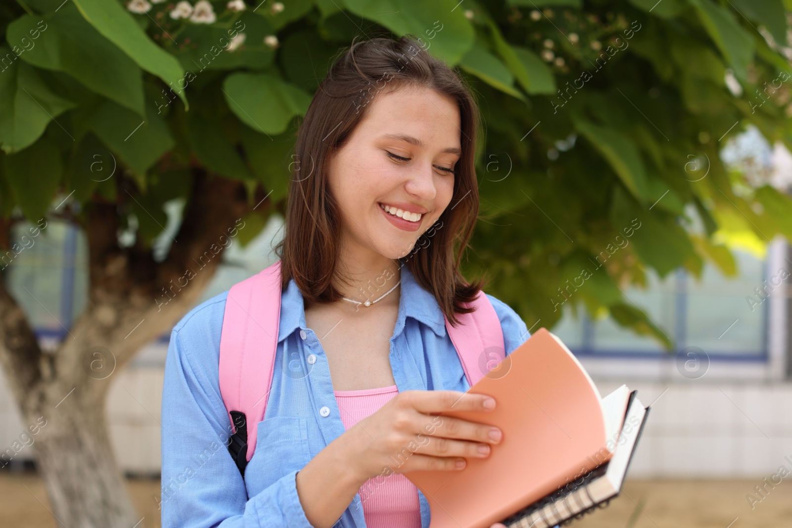 Smiling teenage girl with notebooks near tree outdoors Photo of Smiling teenage girl with notebooks near tree outdoors