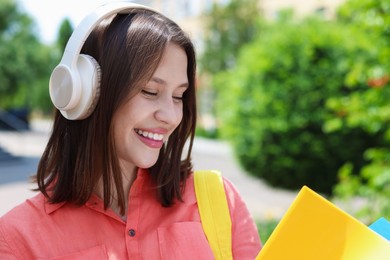 Photo of Smiling teenage girl in headphones reading outdoors