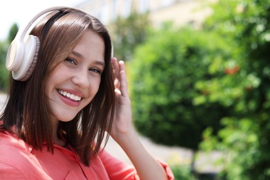 Photo of Smiling teenage girl in headphones listening to music outdoors. Space for text