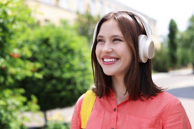 Photo of Smiling teenage girl in headphones listening to music outdoors. Space for text