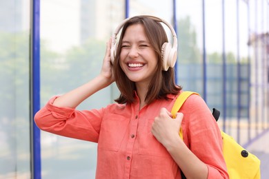 Photo of Smiling teenage girl in headphones listening to music near building outdoors