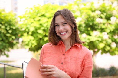 Photo of Smiling teenage girl with notepads on city street