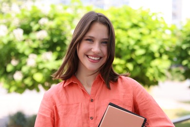 Photo of Portrait of smiling teenage girl with notepads outdoors