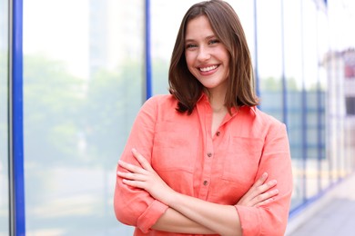 Photo of Portrait of smiling teenage girl with crossed arms near building outdoors