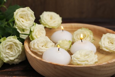 Photo of Burning candles, water and rose flowers in bowl on wooden table, closeup