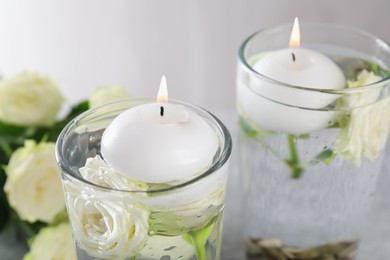 Photo of Burning candles in glasses with water and rose flowers on table, closeup