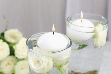 Photo of Burning candles in glasses with water and rose flowers on table, closeup