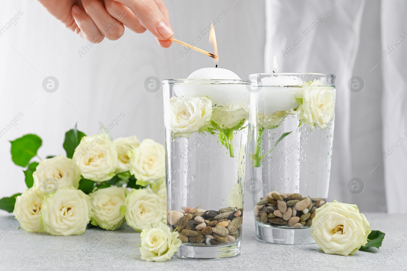 Woman lighting candles in glasses of water at light grey table, closeup Photo of Woman lighting candles in glasses of water at light grey table, closeup