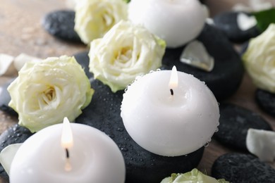 Photo of Burning candles, stones and rose flowers on wooden table, closeup