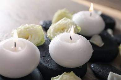 Photo of Burning candles, stones and rose flowers on wooden table, closeup