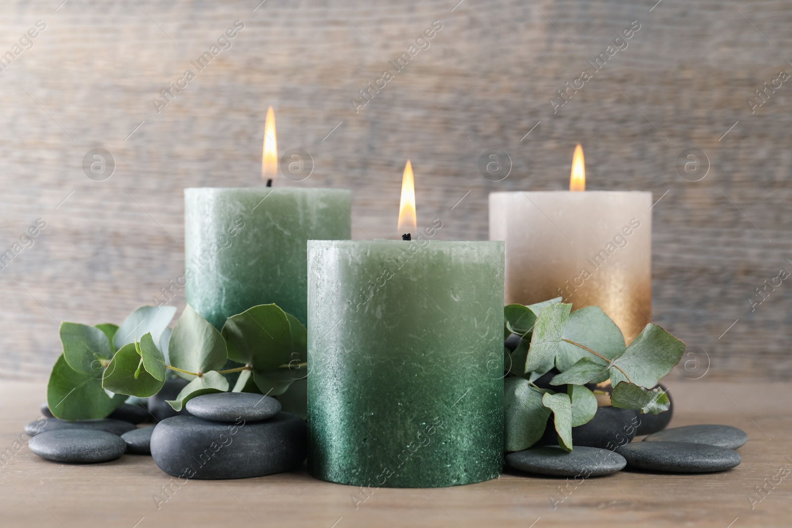 Photo of Burning candles, stones and eucalyptus branches on wooden table, closeup