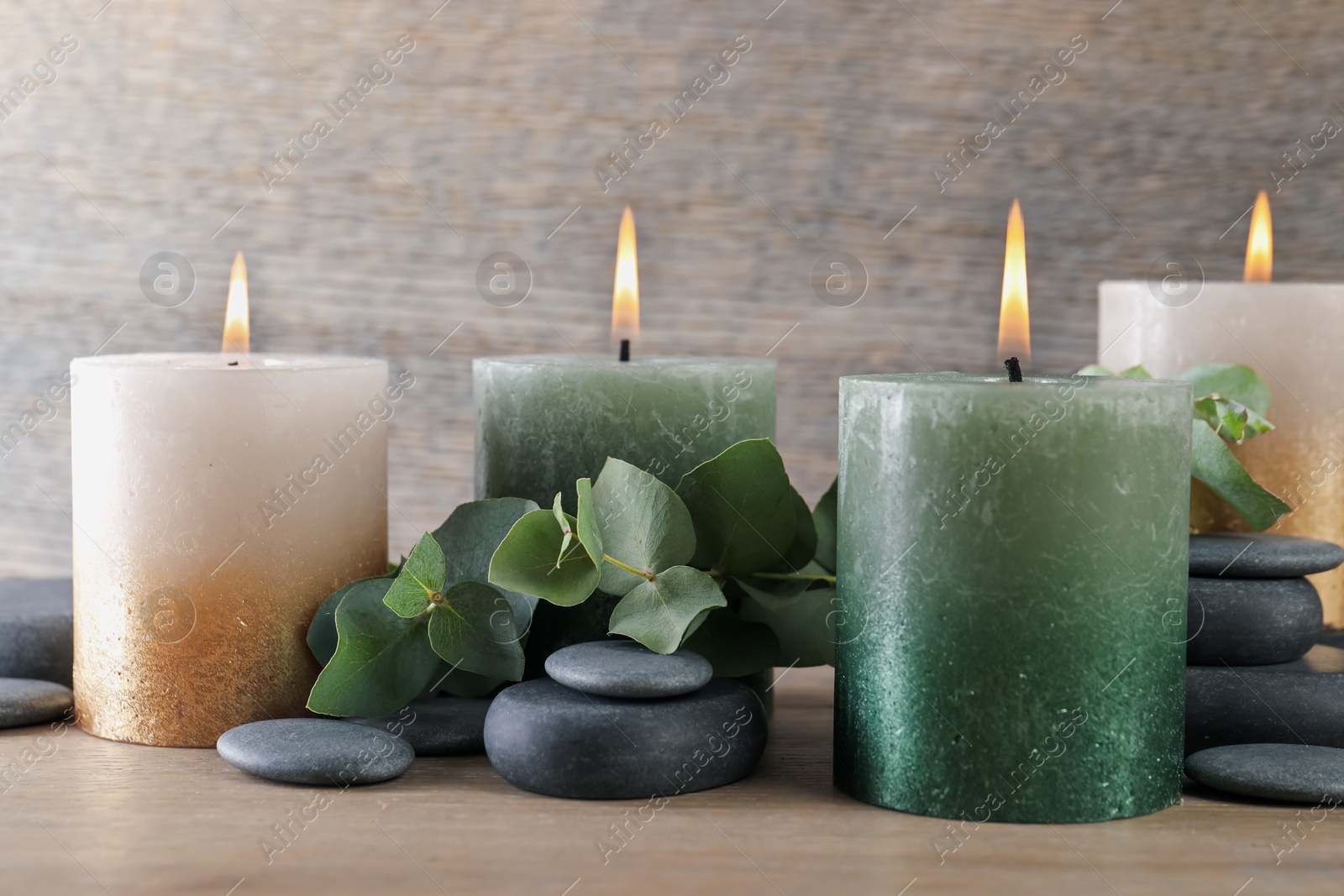 Photo of Burning candles, stones and eucalyptus branches on wooden table, closeup